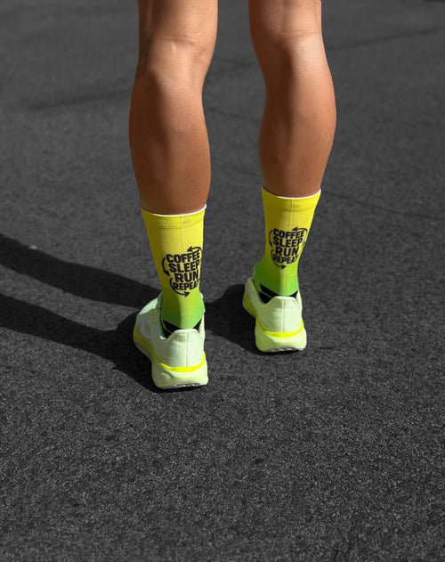 Nahtlose, gelbe Laufsocken mit schwarzem Text "Coffee Sleep Run Repeat" für Marathon und Asphalt.